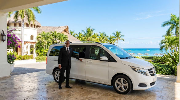 Professional chauffeur opening a white minivan door at a tropical resort in Bayahibe