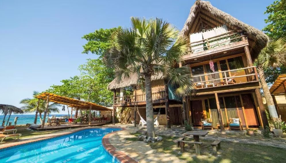 Outdoor swimming pool and bubbling jacuzzi in front of eco-friendly thatched-roof cabins at Cabarete Ecolodge