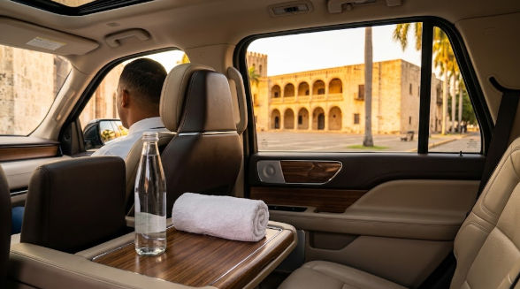 Vista interior de un vehículo de lujo con chofer privado, agua y toalla, con un edificio histórico de Santo Domingo visible a través de la ventana