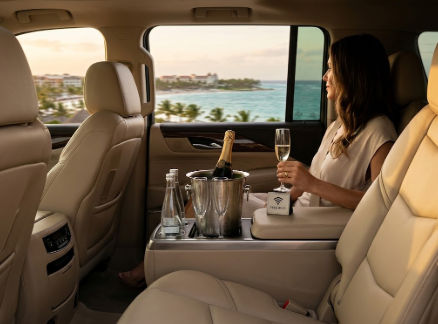 Interior of luxury transfer with woman enjoying champagne and a scenic coastal resort view.