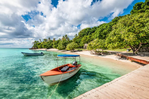 Small motorboat docked by a wooden pier on a tropical beach with clear turquoise water and lush green trees