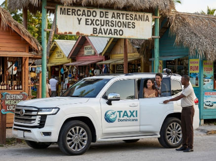 A smiling tourist gets into a white Taxi Dominicana SUV in front of the Bavaro Crafts and Excursions Market.