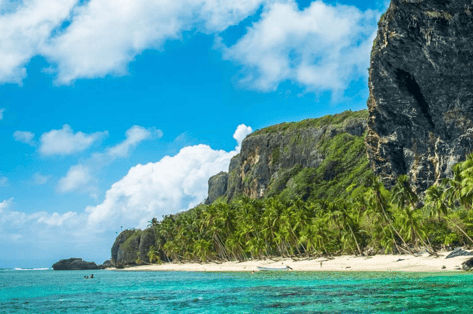 Stunning tropical coastline of Las Terrenas with turquoise ocean, white sand beach, palm trees, and sheer cliffs in Dominican Republic.