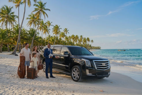 Black luxury SUV transfer vehicle with chauffeur assisting family with luggage on a Dominican Republic beach.