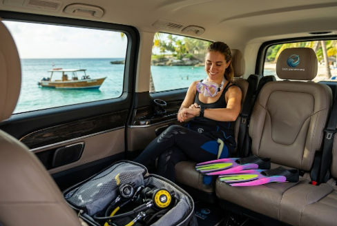 Happy female scuba diver with her gear sitting comfortably inside a private transport vehicle checking her dive watch