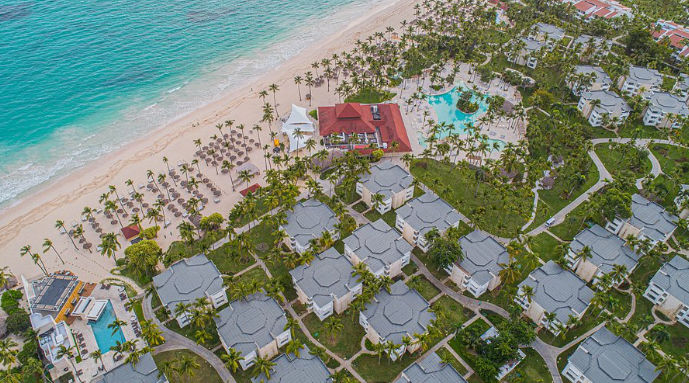 Vista aérea de un extenso resort frente a la playa con múltiples edificios, piscinas, áreas verdes y mar turquesa