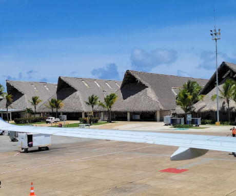 View from an airplane window of a tropical airport terminal with thatched roofs and palm trees
