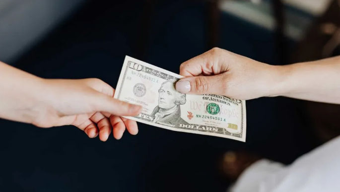 Two hands exchanging a US $10 bill