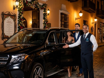 Chofer de transporte VIP abre la puerta de un SUV negro para una pareja que llega a su cena de Nochebuena en Santo Domingo