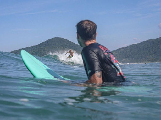 Un surfista observa a otro montando una ola en la costa de Cabarete, República Dominicana, con montañas de fondo