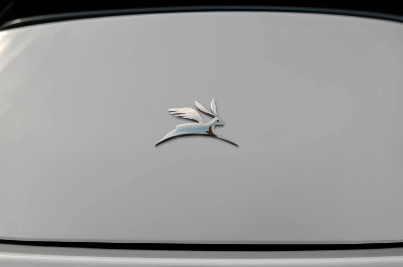 Polished chrome winged rabbit emblem centered on a minimalist white curved automotive vehicle surface.