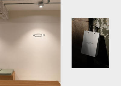 Minimalist brand logo on a white interior wall and a silver shopping bag.