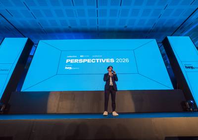 Keynote speaker presenting on stage in front of a massive LED backdrop with electric blue perspective grid lines.