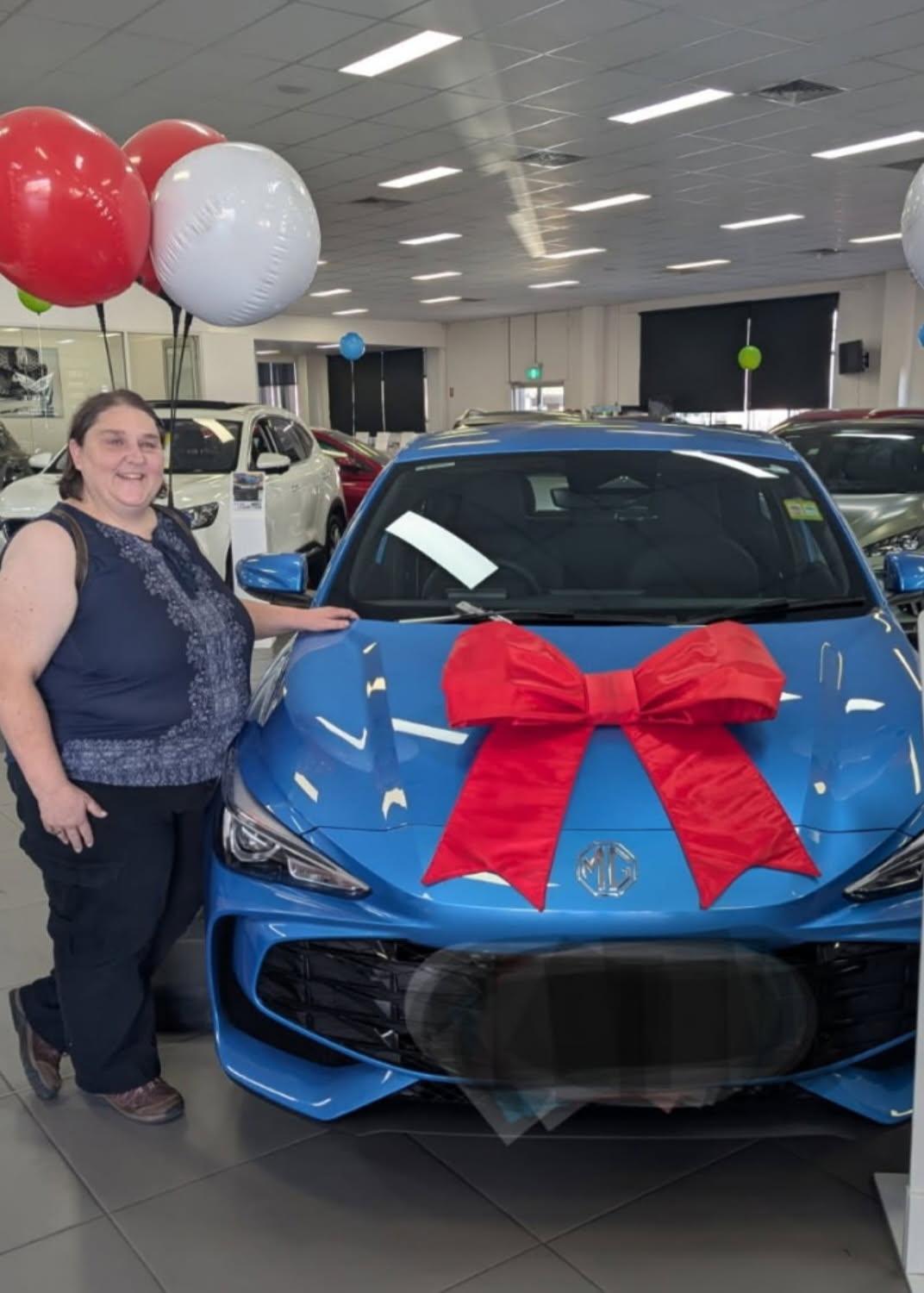 Customer standing next to blue car with red bow in dealership