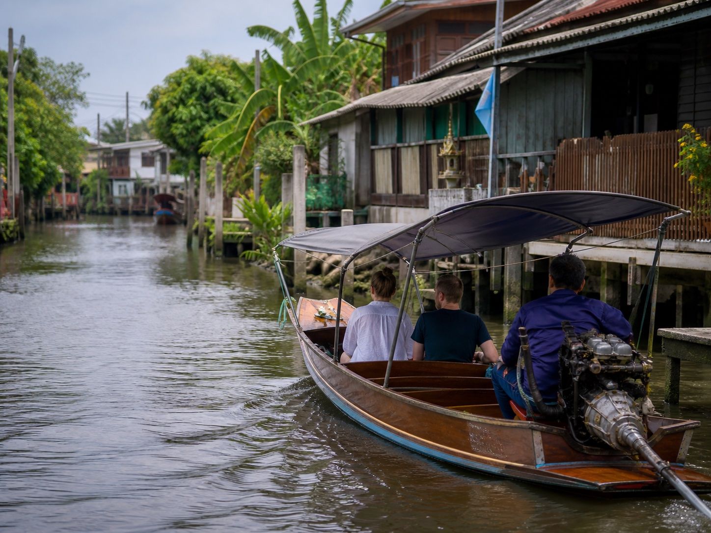 International travellers seated safely in a long-tail boat passing homes along a quiet Thonburi canal