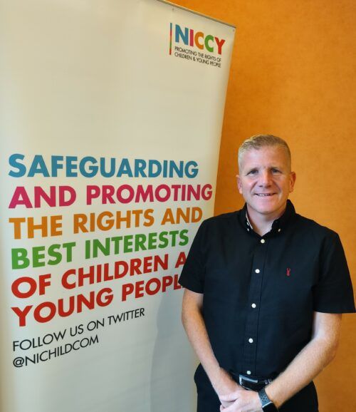 Chris Quinn, NI Children's Commissioner standing beside a NICCY popup