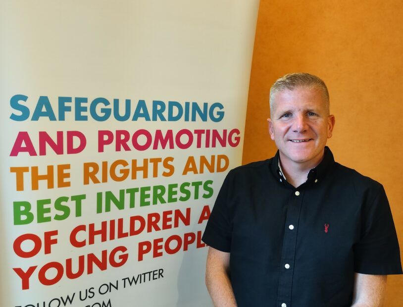 Chris Quinn, NI Children's Commissioner standing beside a NICCY popup