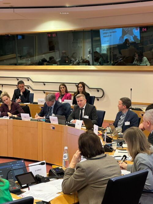 This is a photo of Commissioner Chris Quinn speaking in a conference room at the European Parliament. There are people sitting at desks and they are listening to Chris speak. He is also seated.