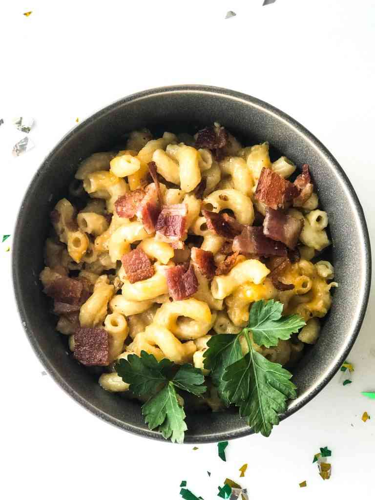 macaroni and cheese in a grey bowl with bits of bacon on top and a sprig of parsley to garnish.