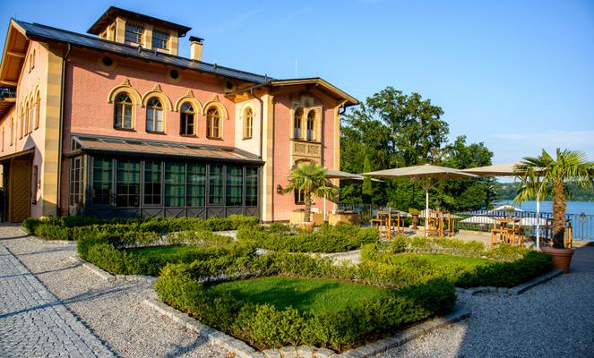 Ein historisches Gebäude mit Garten und Sonnenschirmen auf der Terrasse am Wasser.