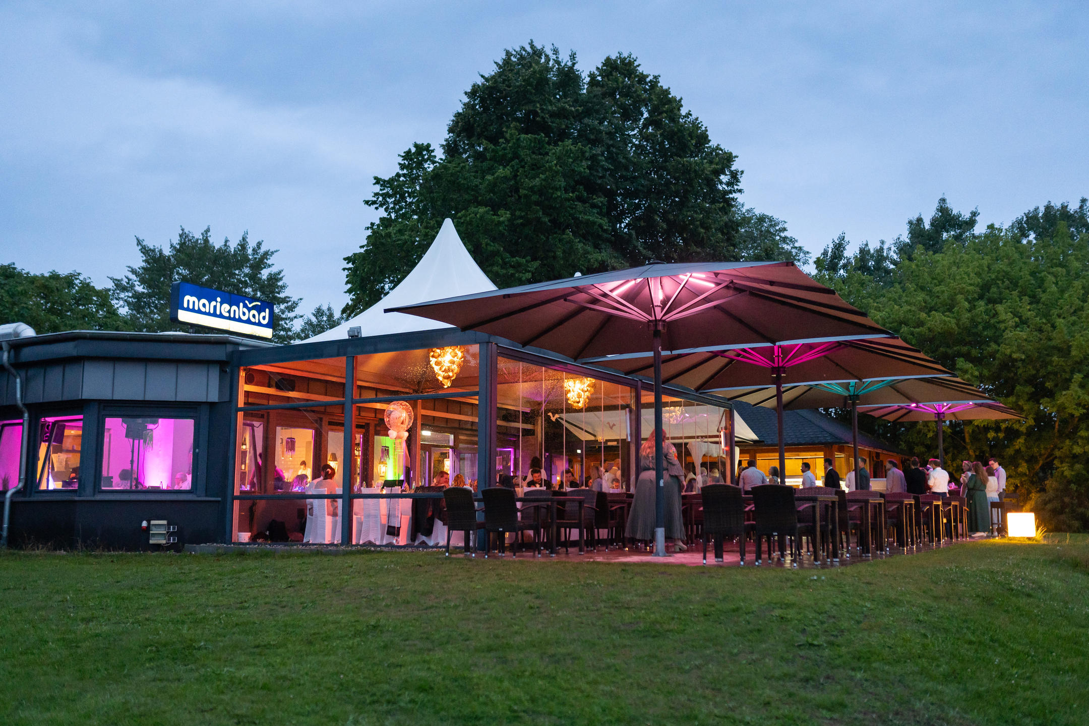 Strand mit weißen Liegestühlen, Strandkörben und großen grauen Sonnenschirmen vor einem Restaurant