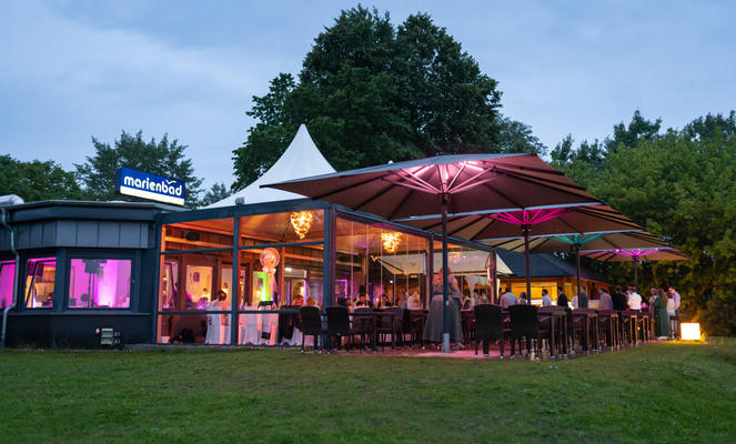 Beach with white deck chairs, beach chairs and large grey parasols in front of a restaurant