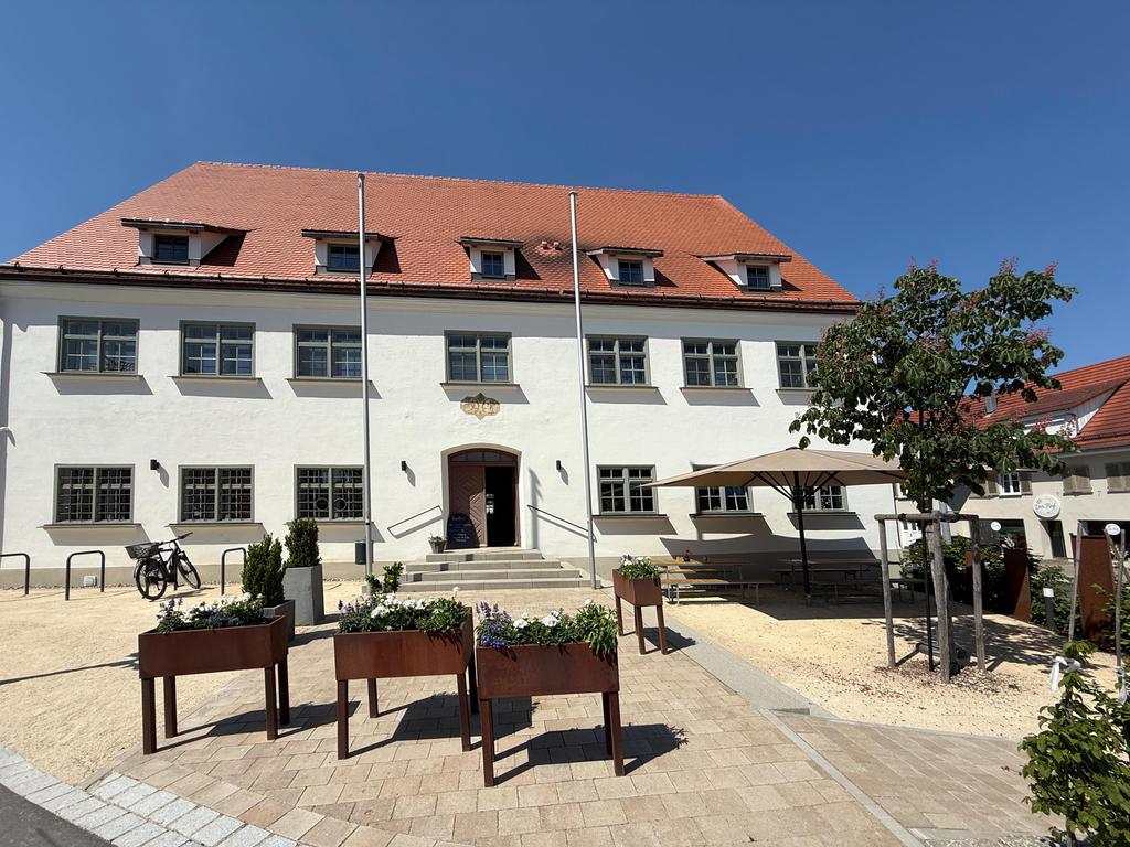 Vue extérieure Le Ruf, bâtiment blanc entretenu avec toit de tuiles rouges et Parasol à l'entrée sous un ciel bleu
