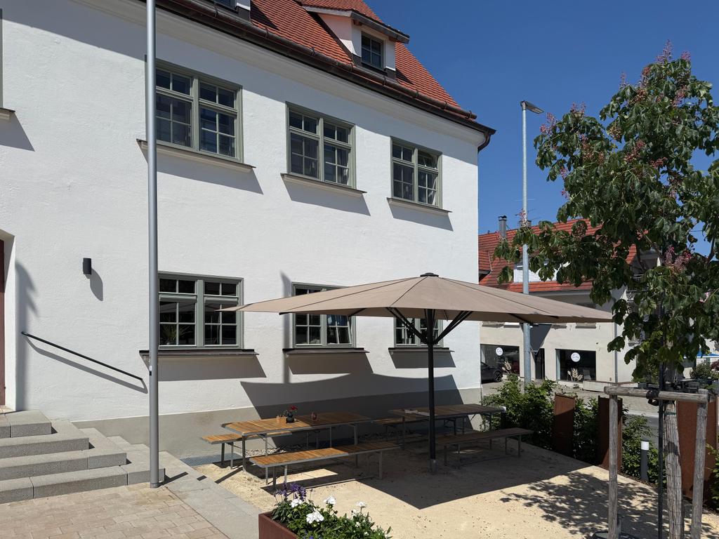 Vue extérieure Le Ruf, bâtiment blanc entretenu avec toit de tuiles rouges et Parasol à l'entrée sous un ciel bleu