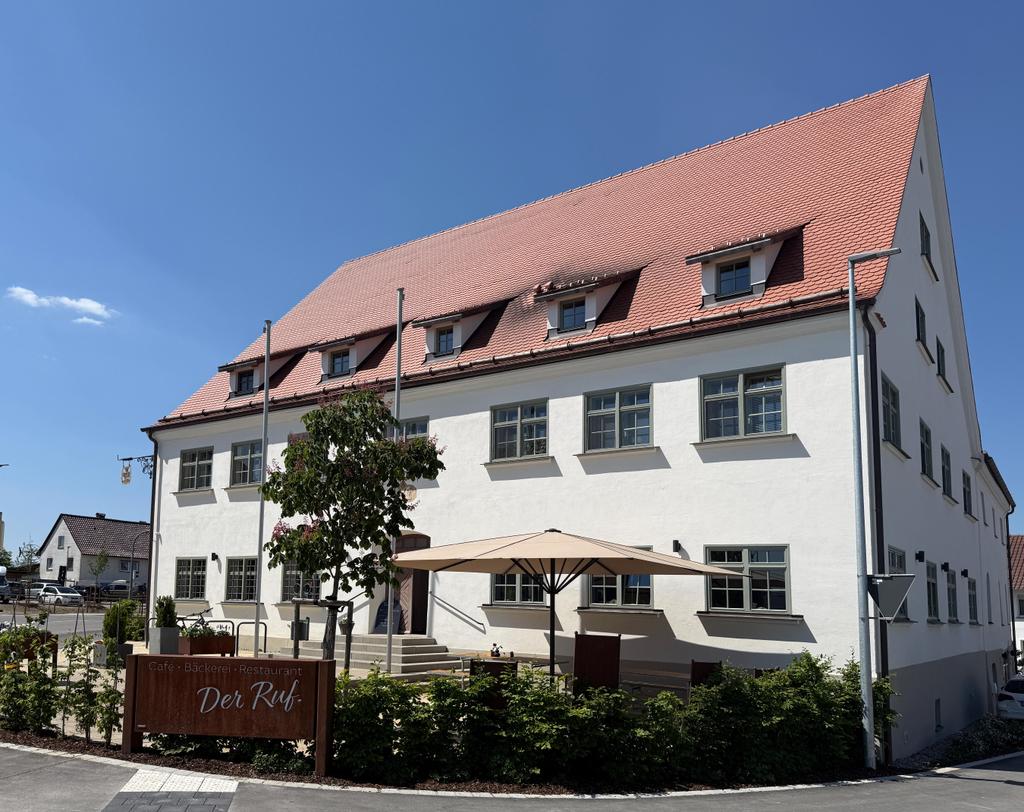 Vue extérieure Le Ruf, bâtiment blanc entretenu avec toit de tuiles rouges et Parasol à l'entrée sous un ciel bleu
