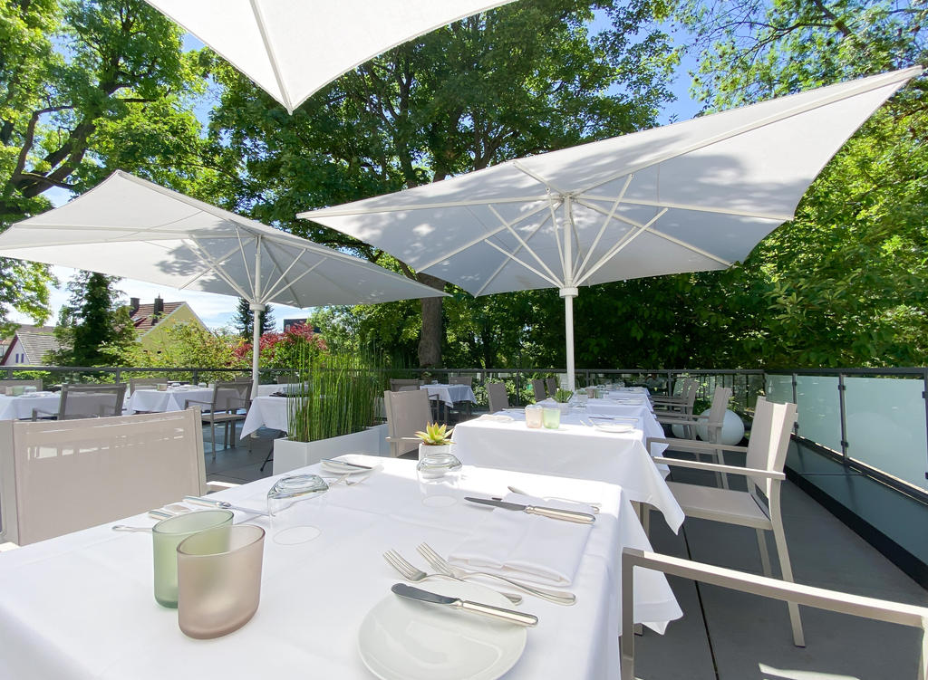 Laudensacks Parkhotel & Retreat mit weißen SCHATTELLO Schirmen Ein Garten mit Bäumen und geschwungenen Wegen neben einer Terrasse mit Sonnenschirm
