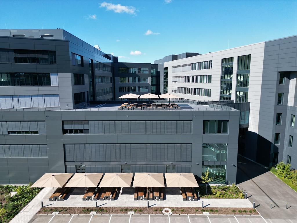 Un immeuble de bureaux moderne avec plusieurs parasols beiges sur la terrasse