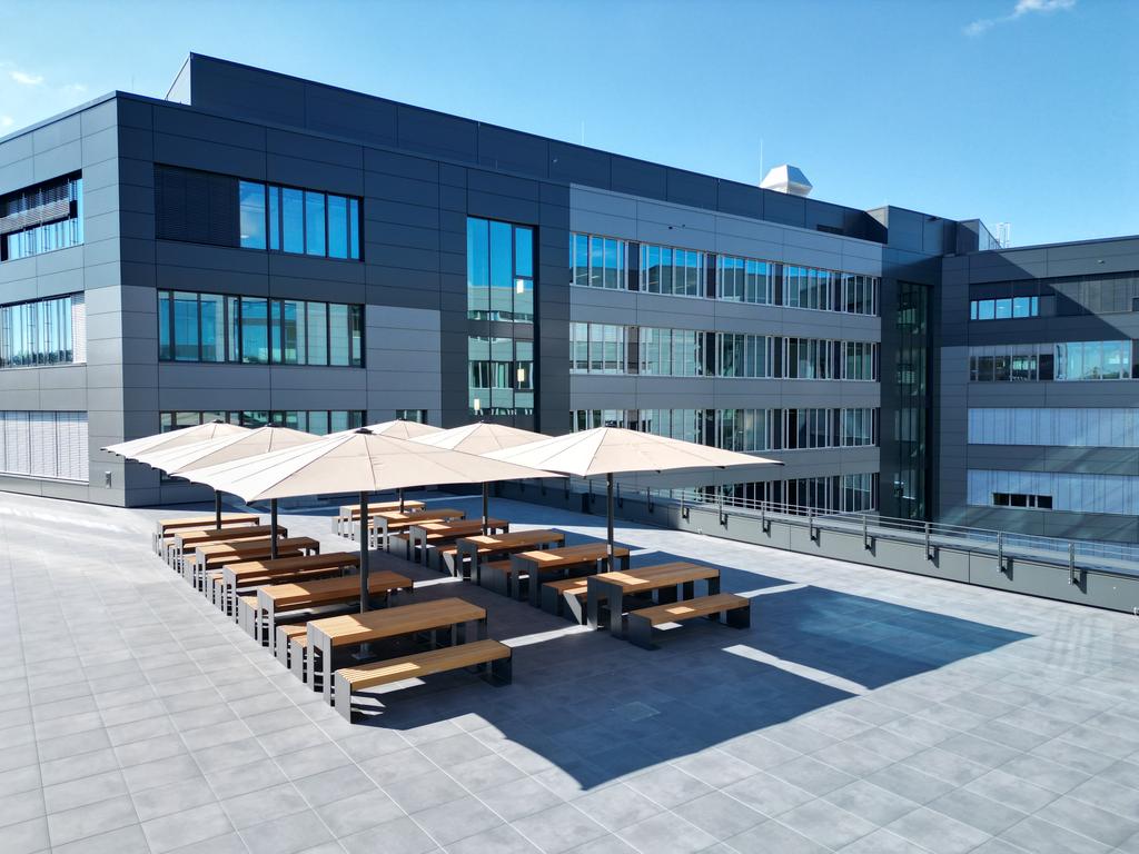Ein modernes Bürogebäude mit mehreren beigen Sonnenschirmen auf der Terrasse