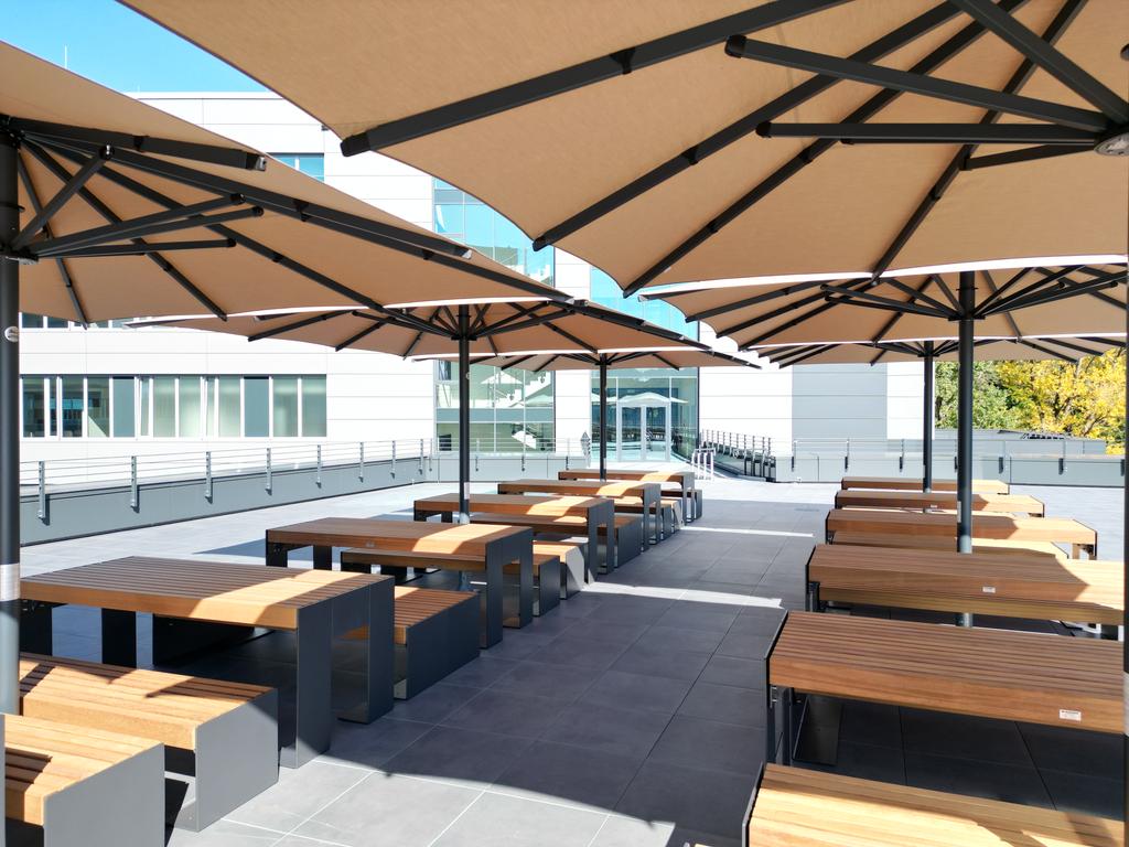 Ein modernes Bürogebäude mit mehreren beigen Sonnenschirmen auf der Terrasse