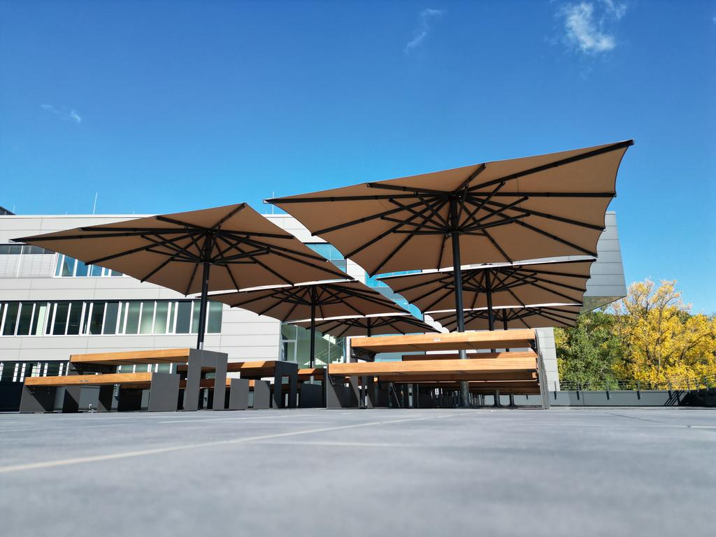 Un immeuble de bureaux moderne avec plusieurs parasols beiges sur la terrasse