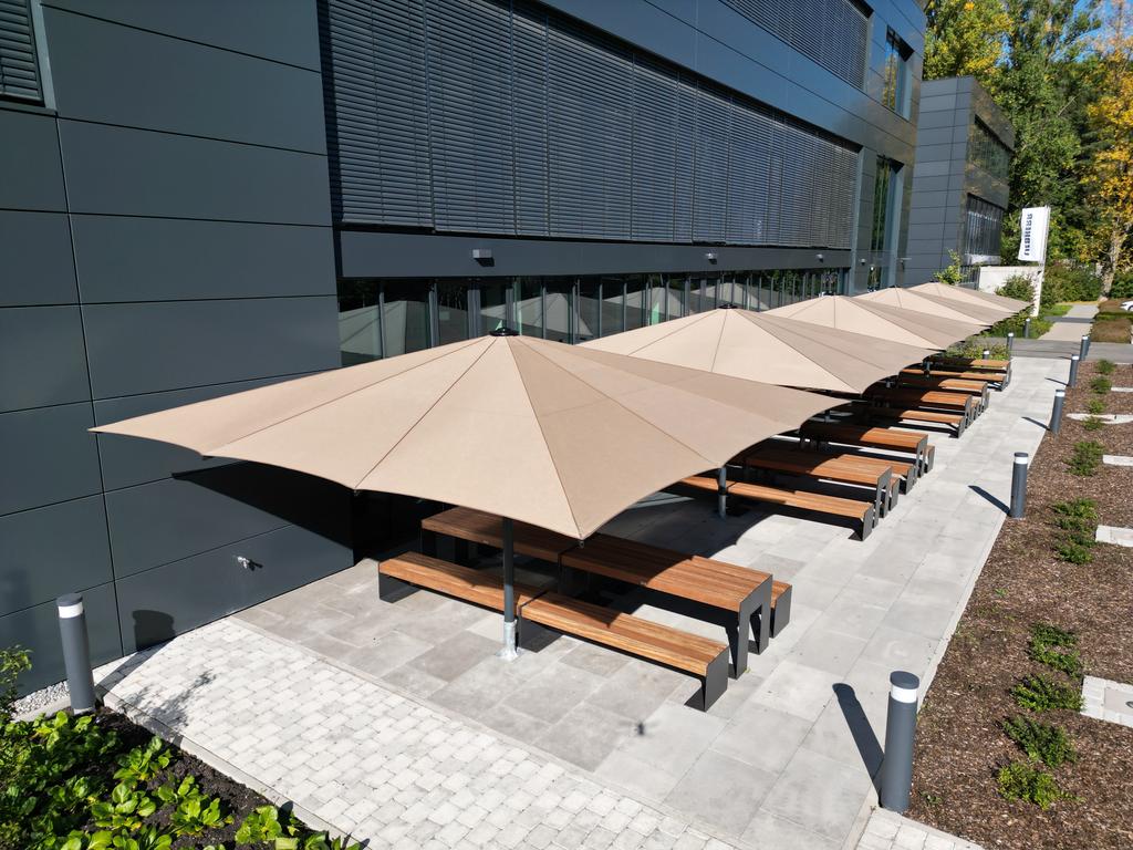 Ein modernes Bürogebäude mit mehreren beigen Sonnenschirmen auf der Terrasse