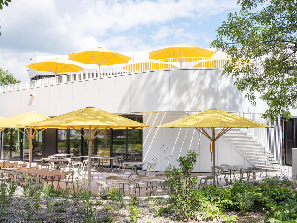 Wagner Markdorf mit gelben SCHATTELLO Schirmen Moderne Terrasse mit gelben Sonnenschirmen neben einem Bürogebäude.