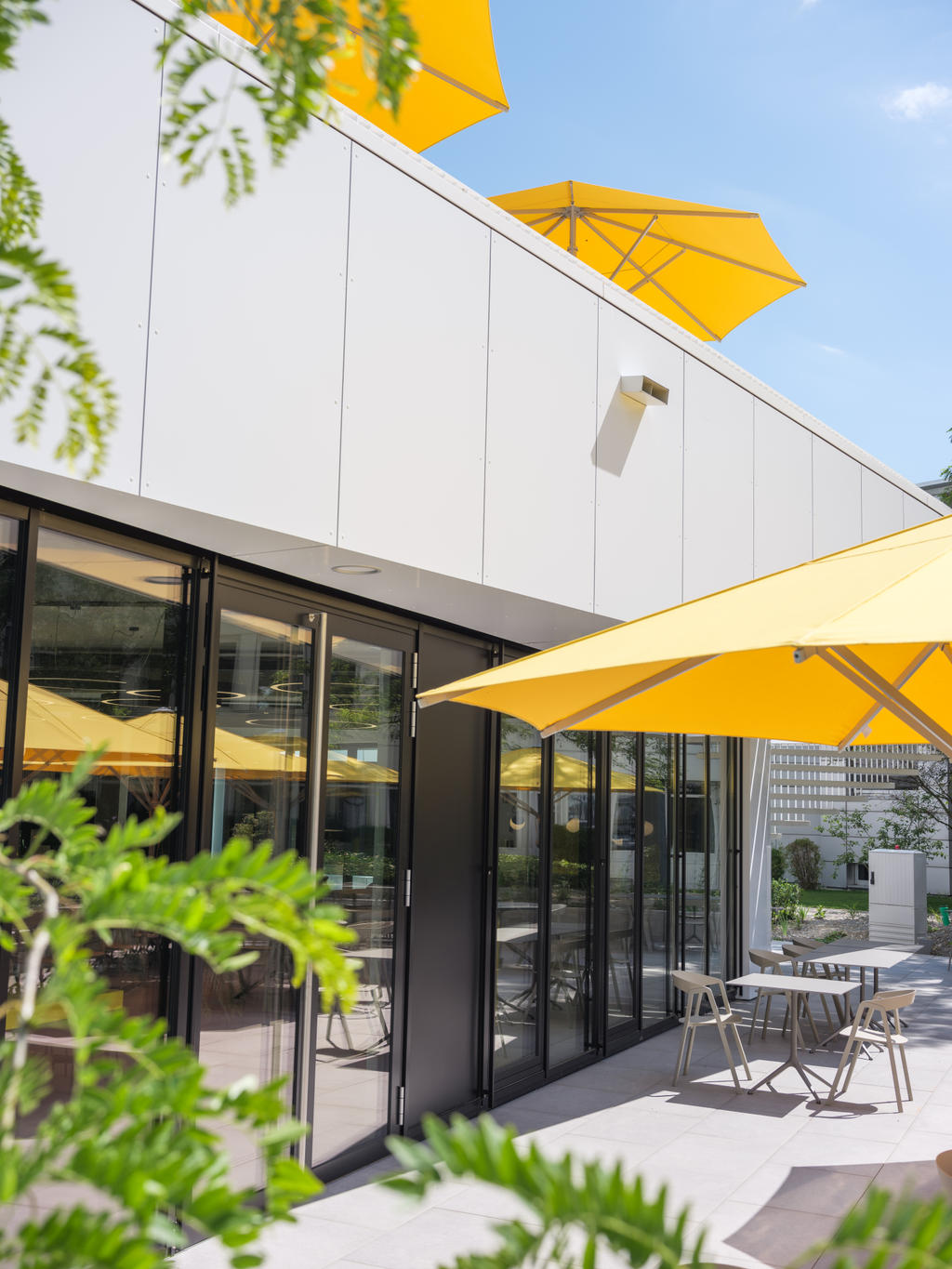 Wagner Markdorf mit gelben SCHATTELLO Schirmen Moderne Terrasse mit gelben Sonnenschirmen neben einem Bürogebäude.