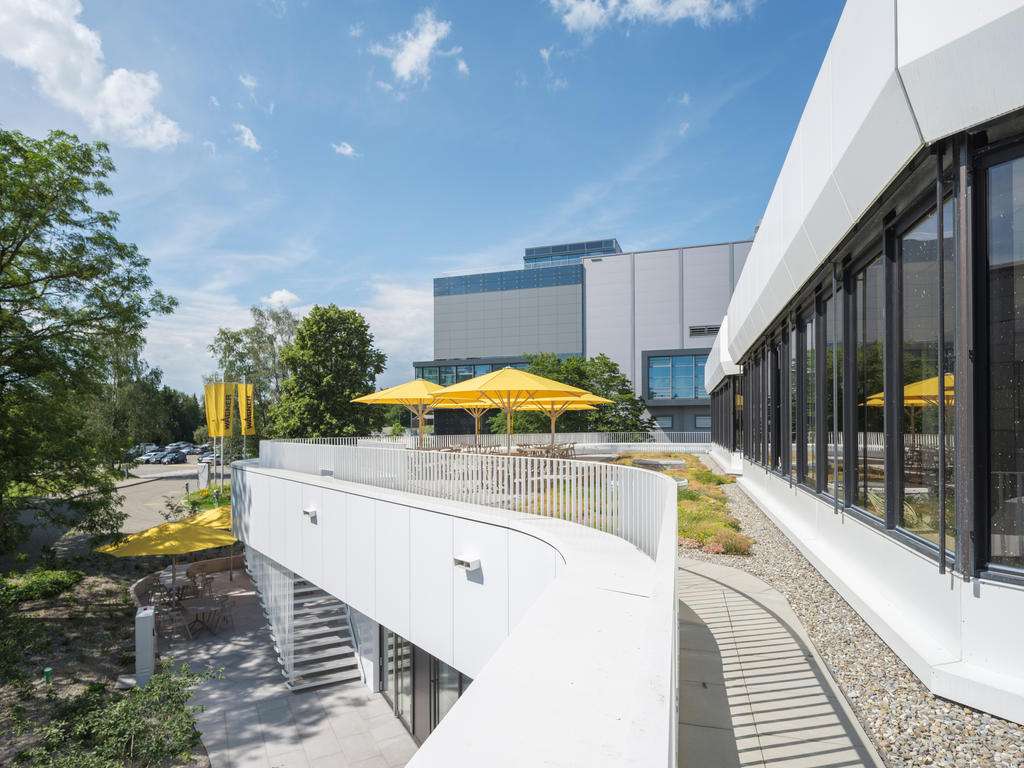 Wagner Markdorf mit gelben SCHATTELLO Schirmen Moderne Terrasse mit gelben Sonnenschirmen neben einem Bürogebäude.