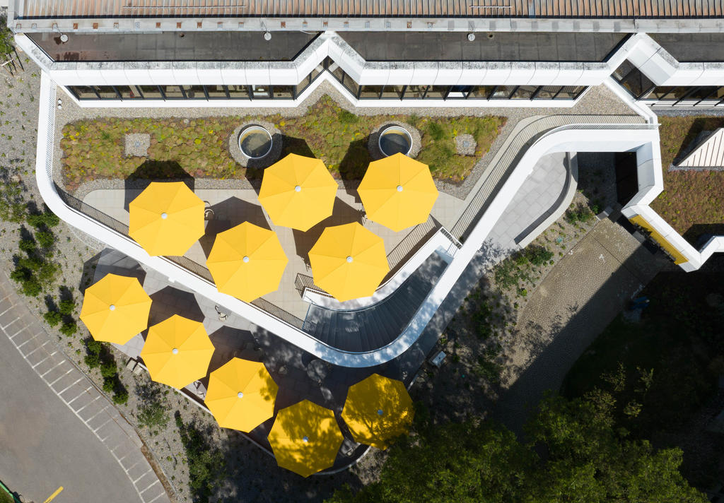 Wagner Markdorf mit gelben SCHATTELLO Schirmen Moderne Terrasse mit gelben Sonnenschirmen neben einem Bürogebäude.