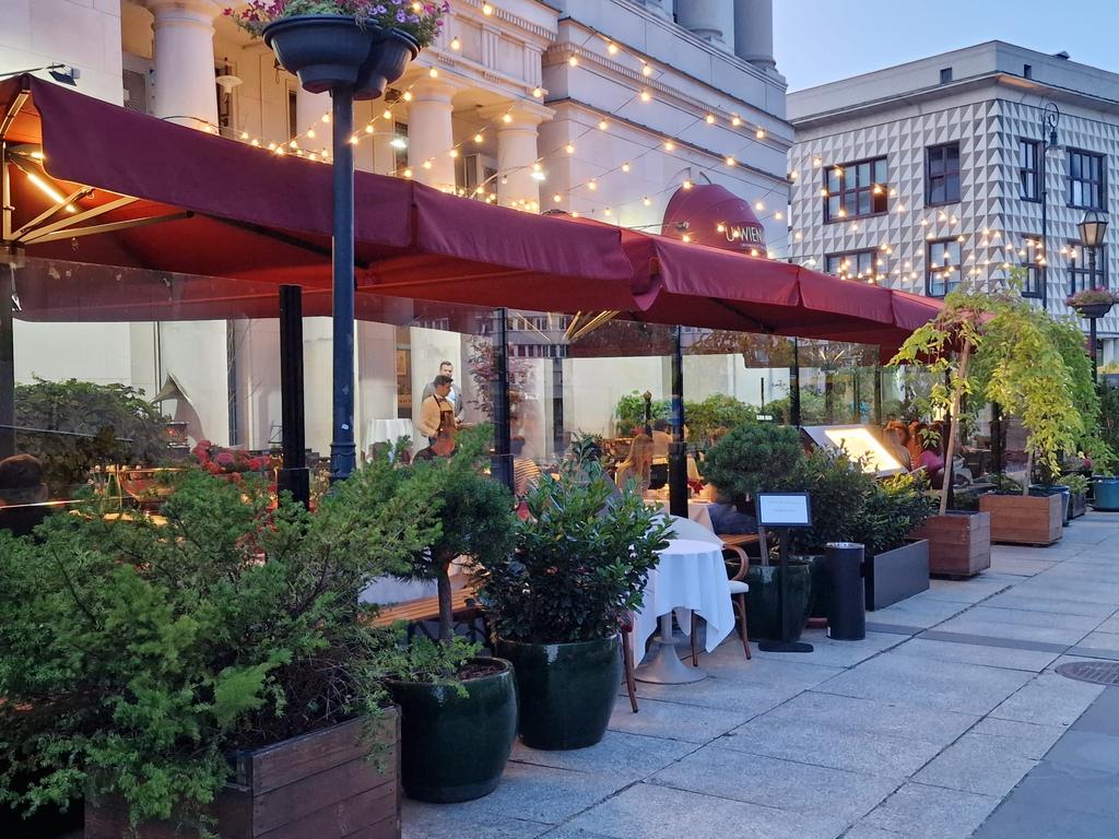 Historisches Gebäude mit Terrasse und roten Sonnenschirmen.