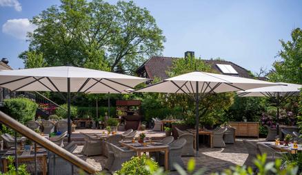 Hofgut avec des parasols rouges SCHATTELLO Une scène de jardin estivale avec des tables en bois décorées et des parasols rouges.