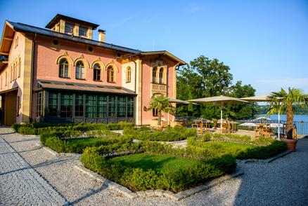 La Villa with beige SCHATTELLO parasols A historic building with a garden and parasols on the terrace by the water.
