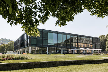 Plenum, Stuttgart avec des parasols SCHATTELLO blancs Un bâtiment moderne en verre avec des parasols blancs le long de la terrasse entourée de verdure