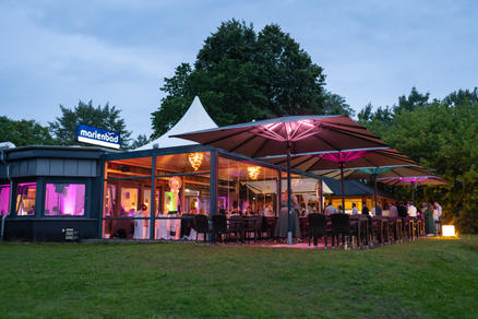 Beach with white deck chairs, beach chairs and large grey parasols in front of a restaurant