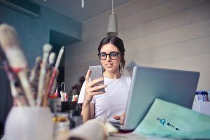 Live-Streaming-101-woman-in-white-t-shirt-holding-smartphone-in-front-of-laptop