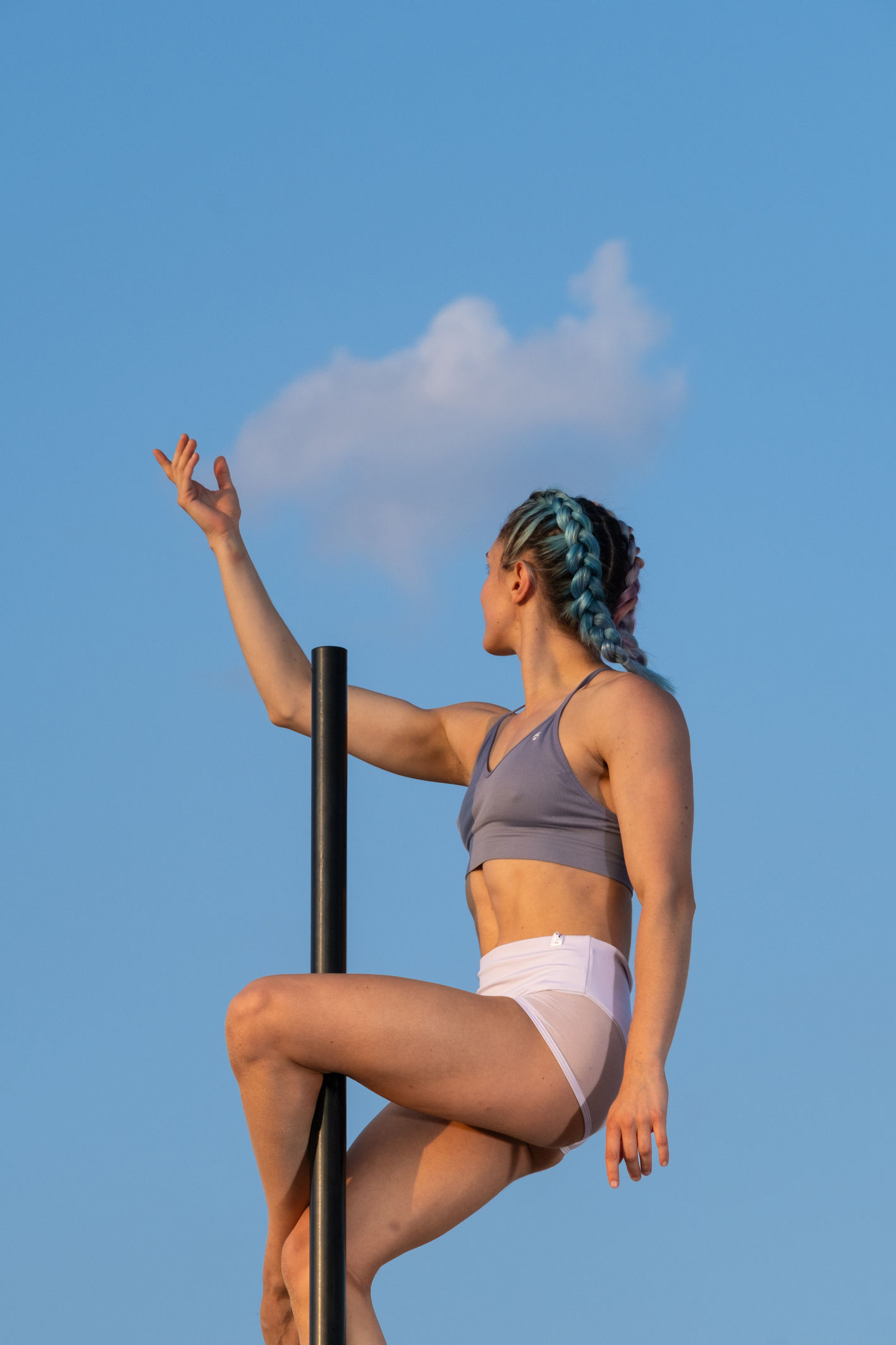 Ballerina seduta in figura su un palo all'aperto contro il cielo azzurro