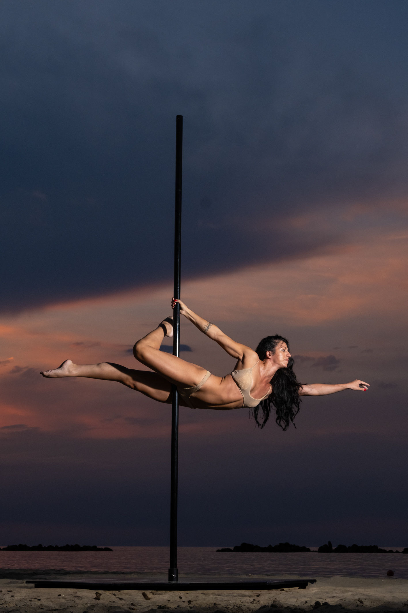 Ballerina in spaccata aerea su un palo, cielo al tramonto sul mare