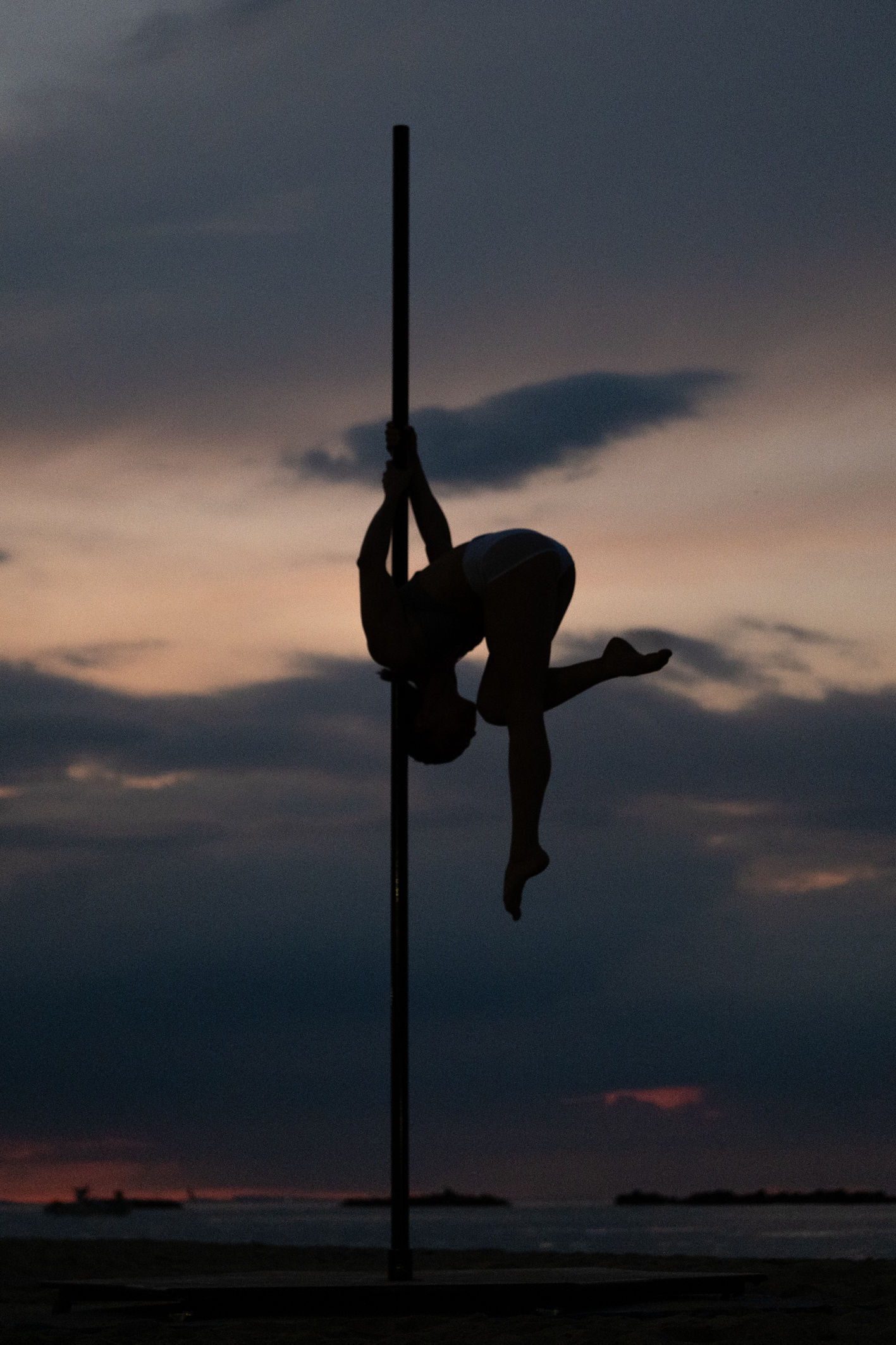 Silhouette di una ballerina raccolta sul palo contro il cielo del tramonto