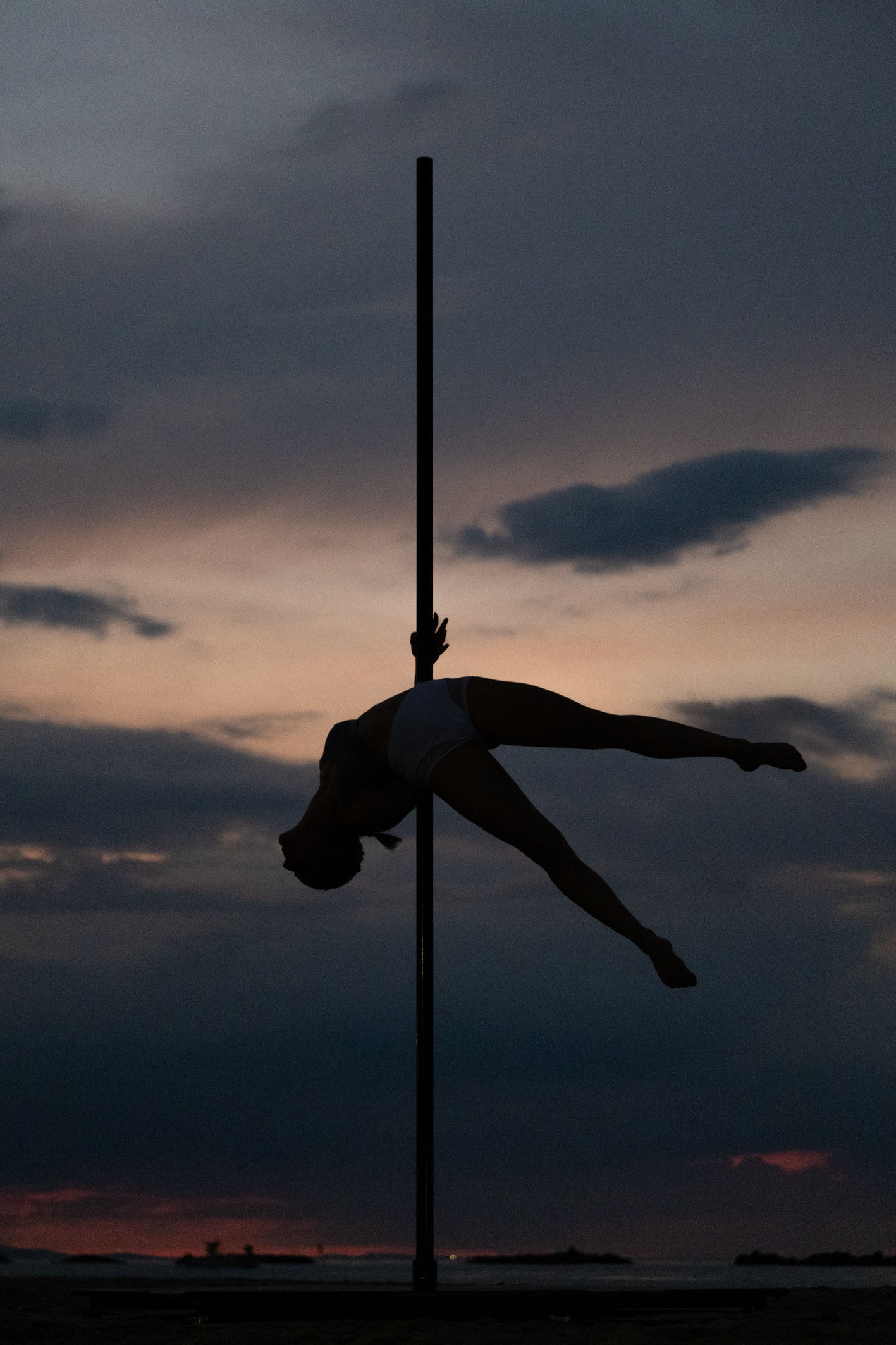 Silhouette di una ballerina distesa in orizzontale sul palo al crepuscolo