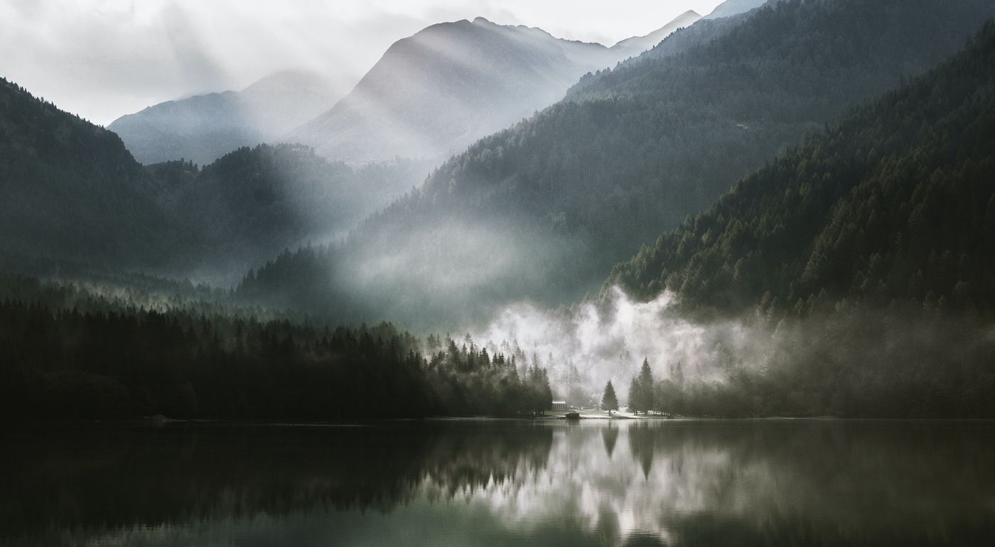 Dark mountains with sun beams and mist coming up from a still lake.